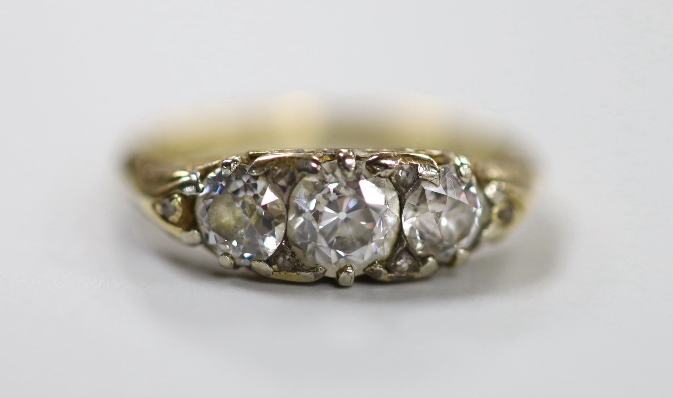 An antique yellow metal and graduated three stone diamond set ring, with diamond chip set spacers, size N/O, gross weight 4 grams